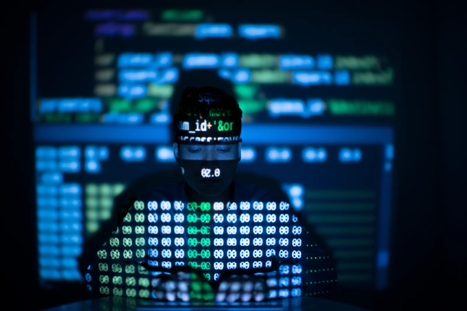 Person vor Bildschirmen mit Programmcode im blauen Licht