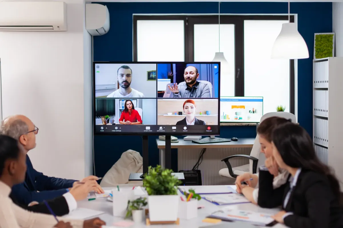 Kleiner Meetingraum mit Videokonferenz auf großem Monitor
